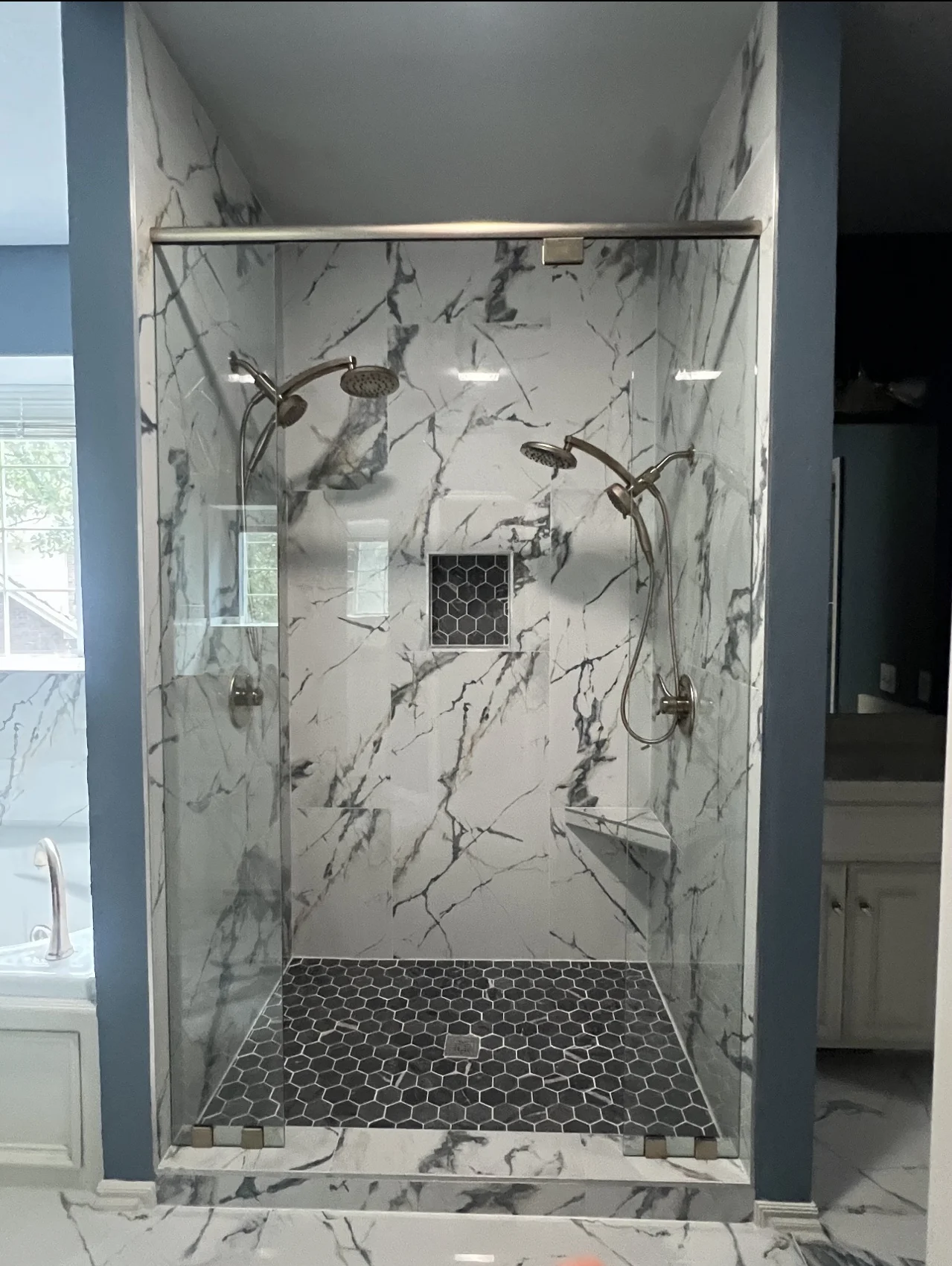 After: shower with large marble-look tile, two shower heads, dark hexagonal floor tile and niche