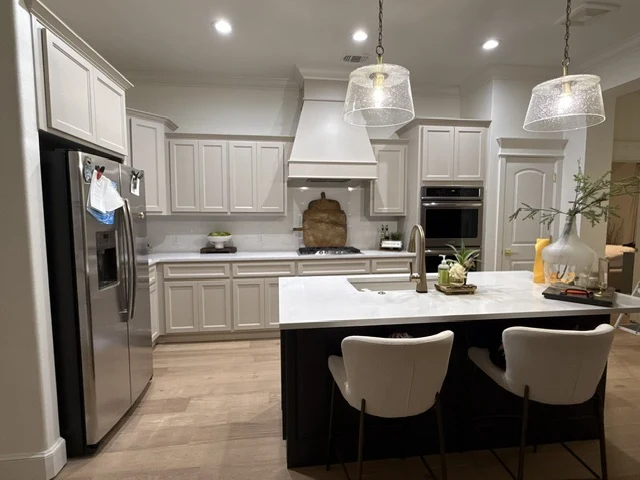 Dusty Project finished kitchen with light cabinetry, dark island, pendant lights and wood-look floors